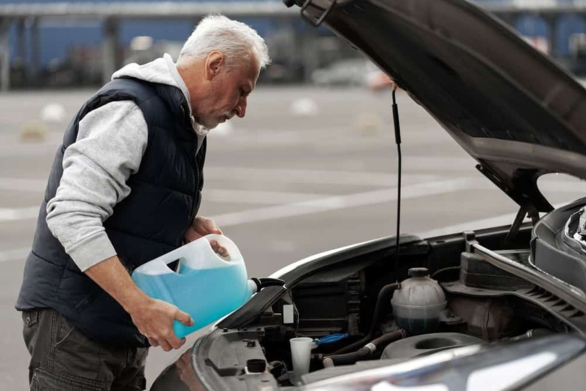 Older man pours coolant into his engine